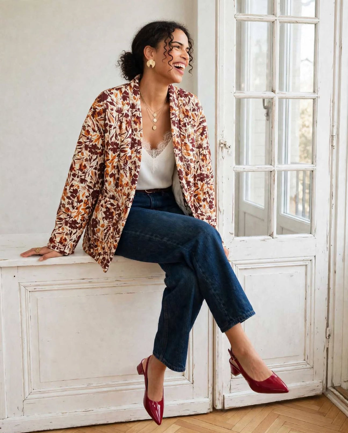 Kimono Flora porté ouvert, modèle assis près d’une fenêtre avec un jean bleu et des chaussures bordeaux.