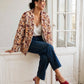 Kimono Flora porté ouvert, modèle assis près d’une fenêtre avec un jean bleu et des chaussures bordeaux.