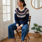 Pull Enora à motif jacquard porté avec un jean bleu, modèle assis sur une chaise.